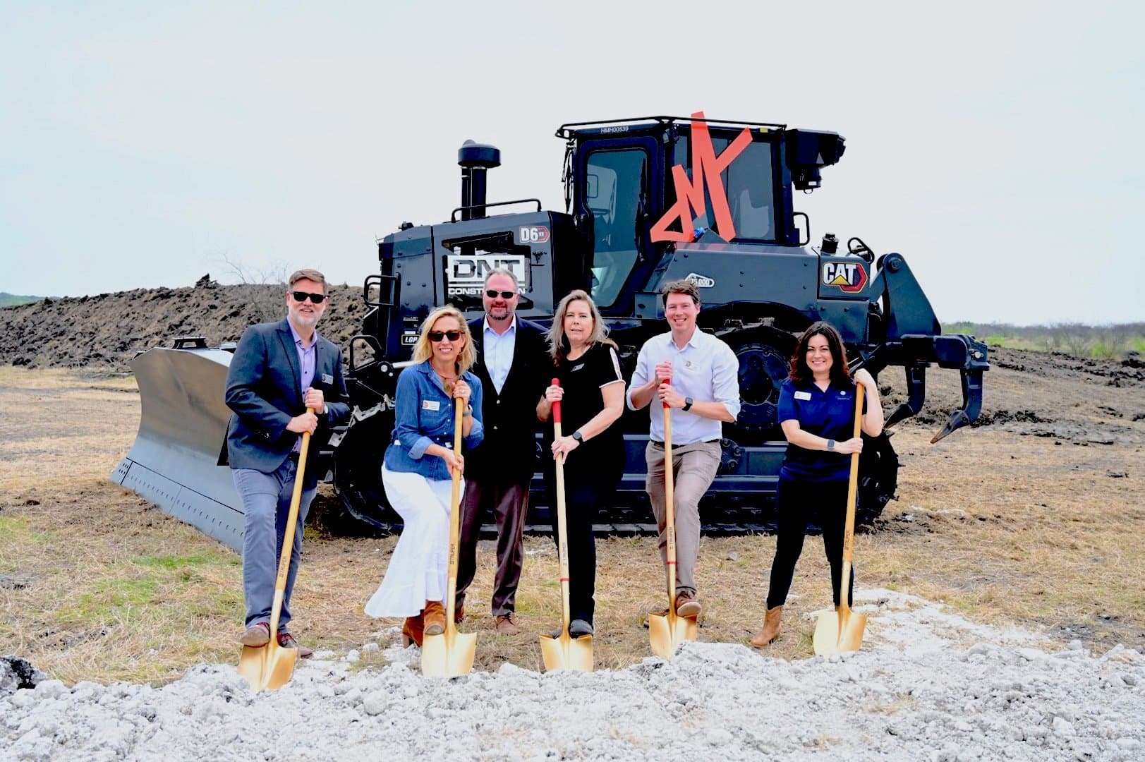 A group of Southstar team members posing with shovels in front of a bulldozer.