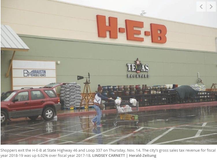 A woman is standing in front of a H E B store.