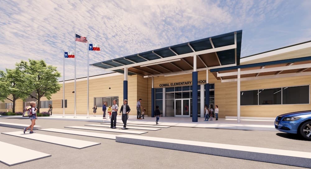 An elementary school entrance with people walking on the crosswalk, three flags on poles, and a blue car parked nearby. The building sign reads "Comal Elementary School.