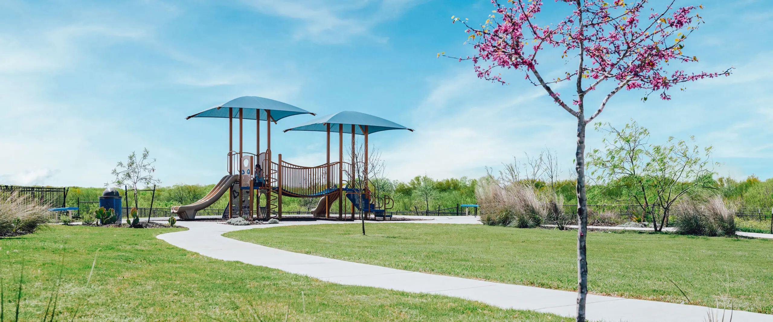 A park with a playground surrounded by trees and green space at Mission del Lago.