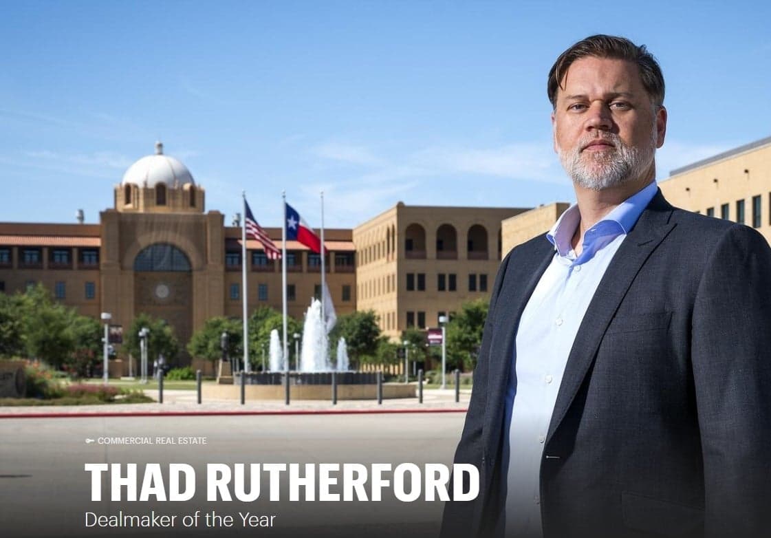 Thad Rutherford in a suit and standing in front of a building.
