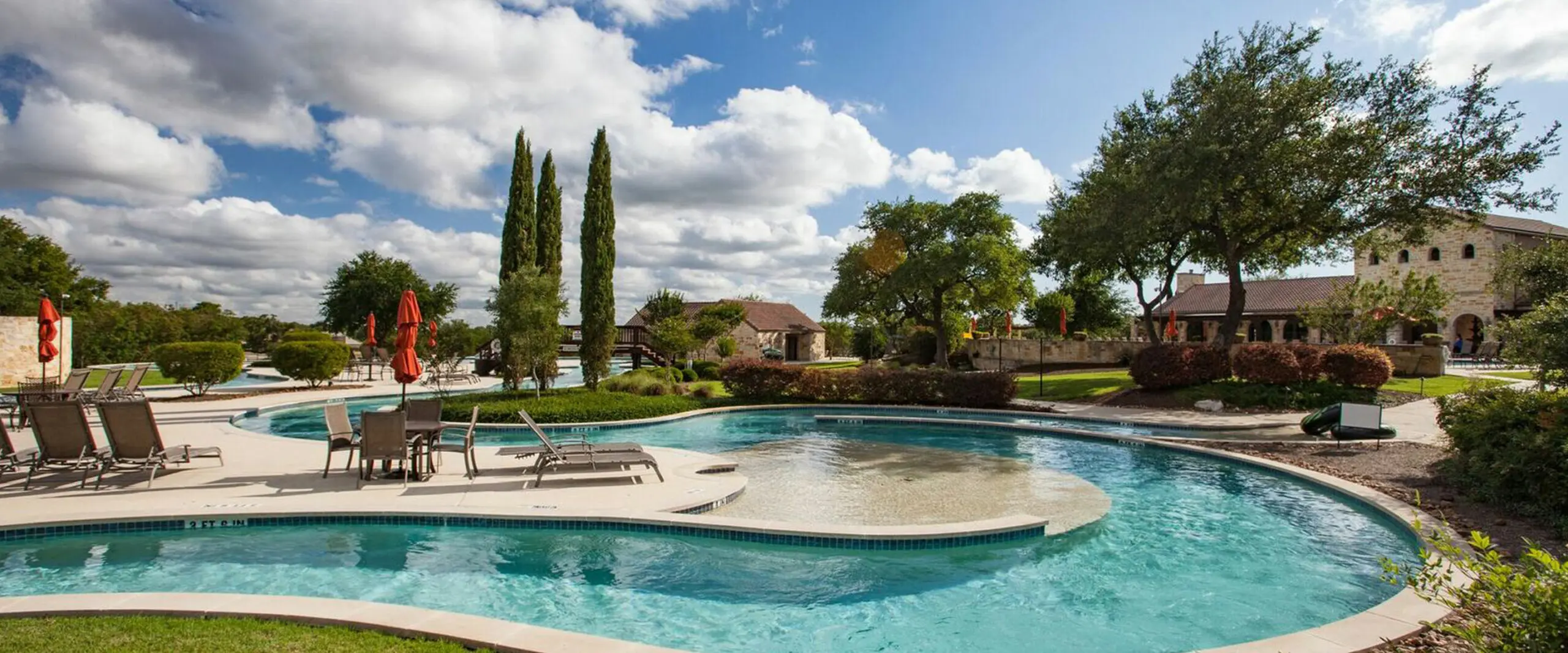A swimming pool with lounge chairs and trees at Vintage Oaks in New Braunfels, Texas