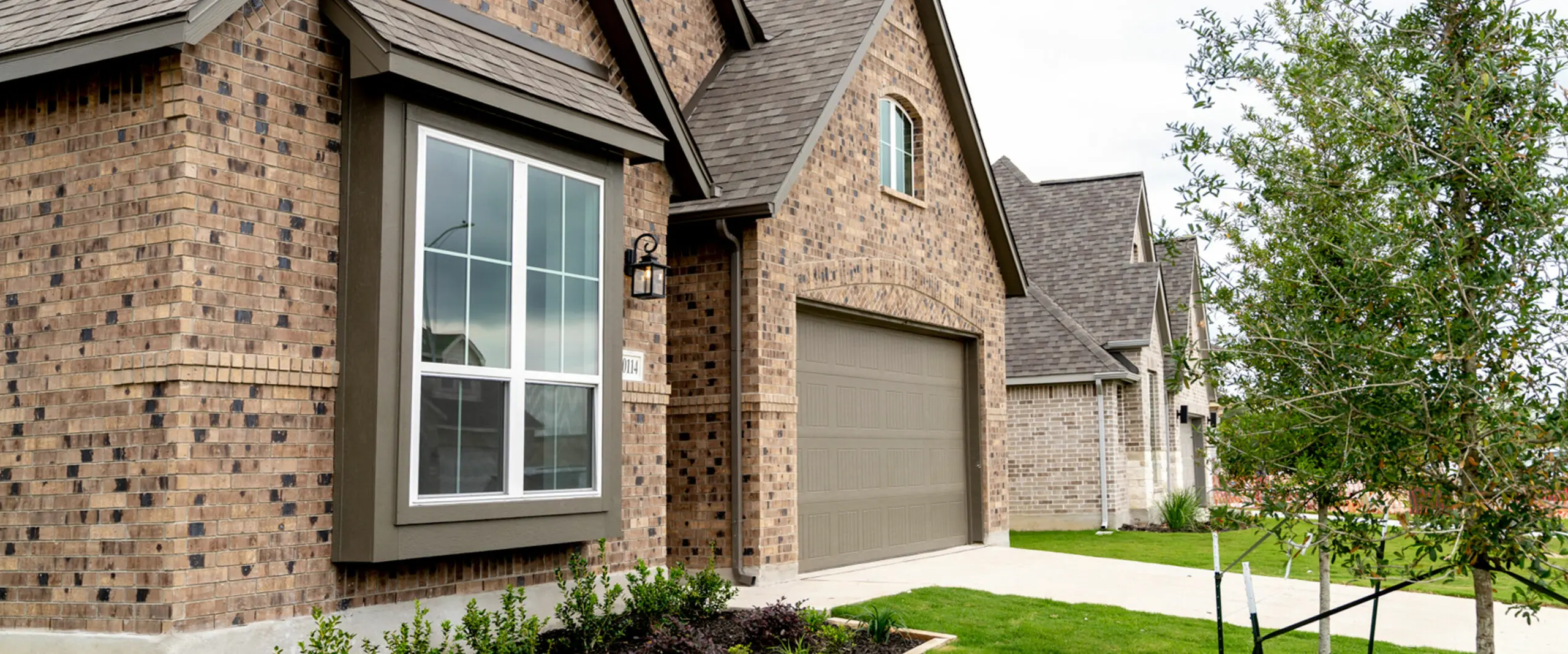 A brown brick house with a garage and grass in front of it.
